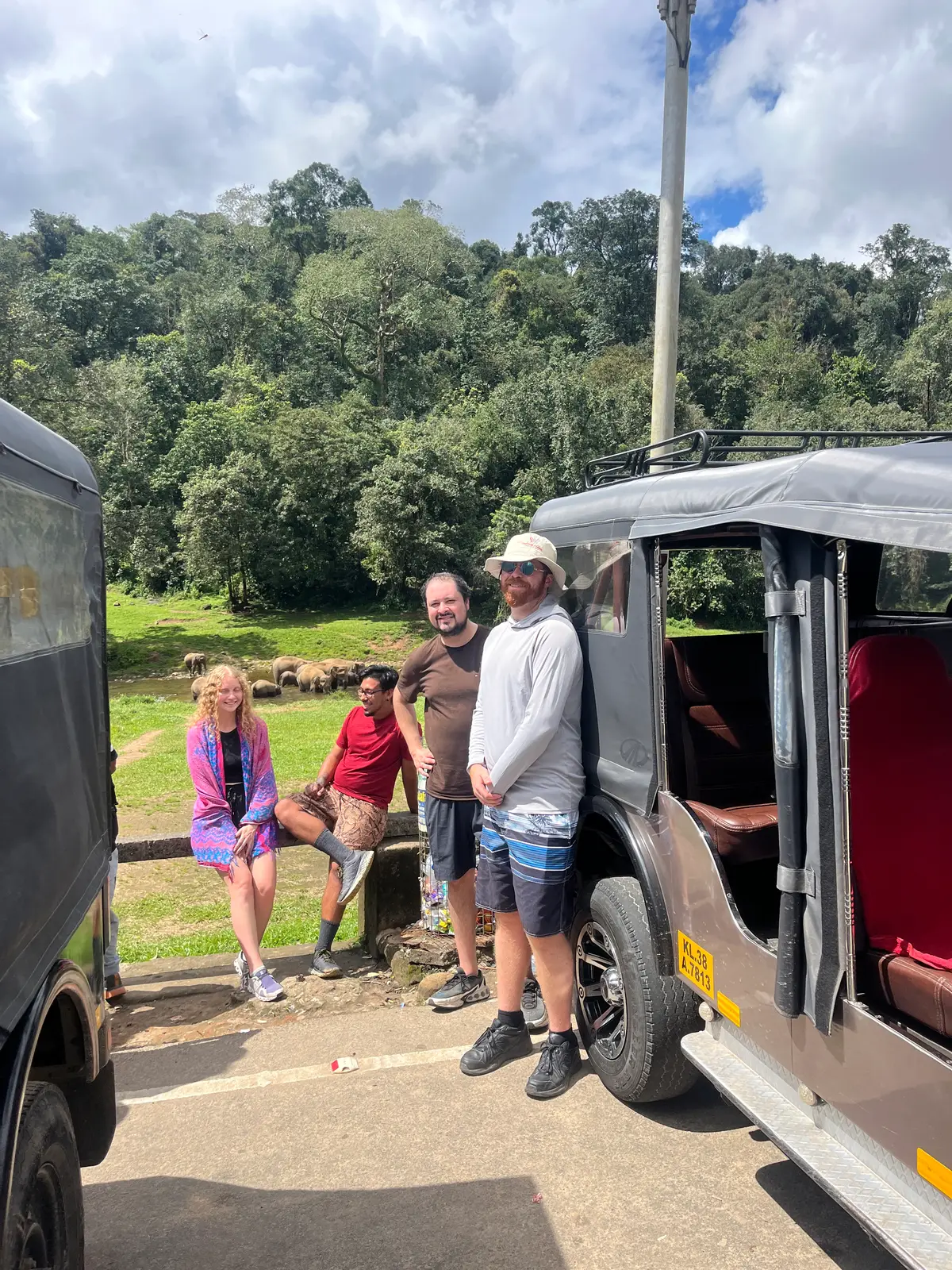 Guests beside a safari jeep watching wild elephants across the river